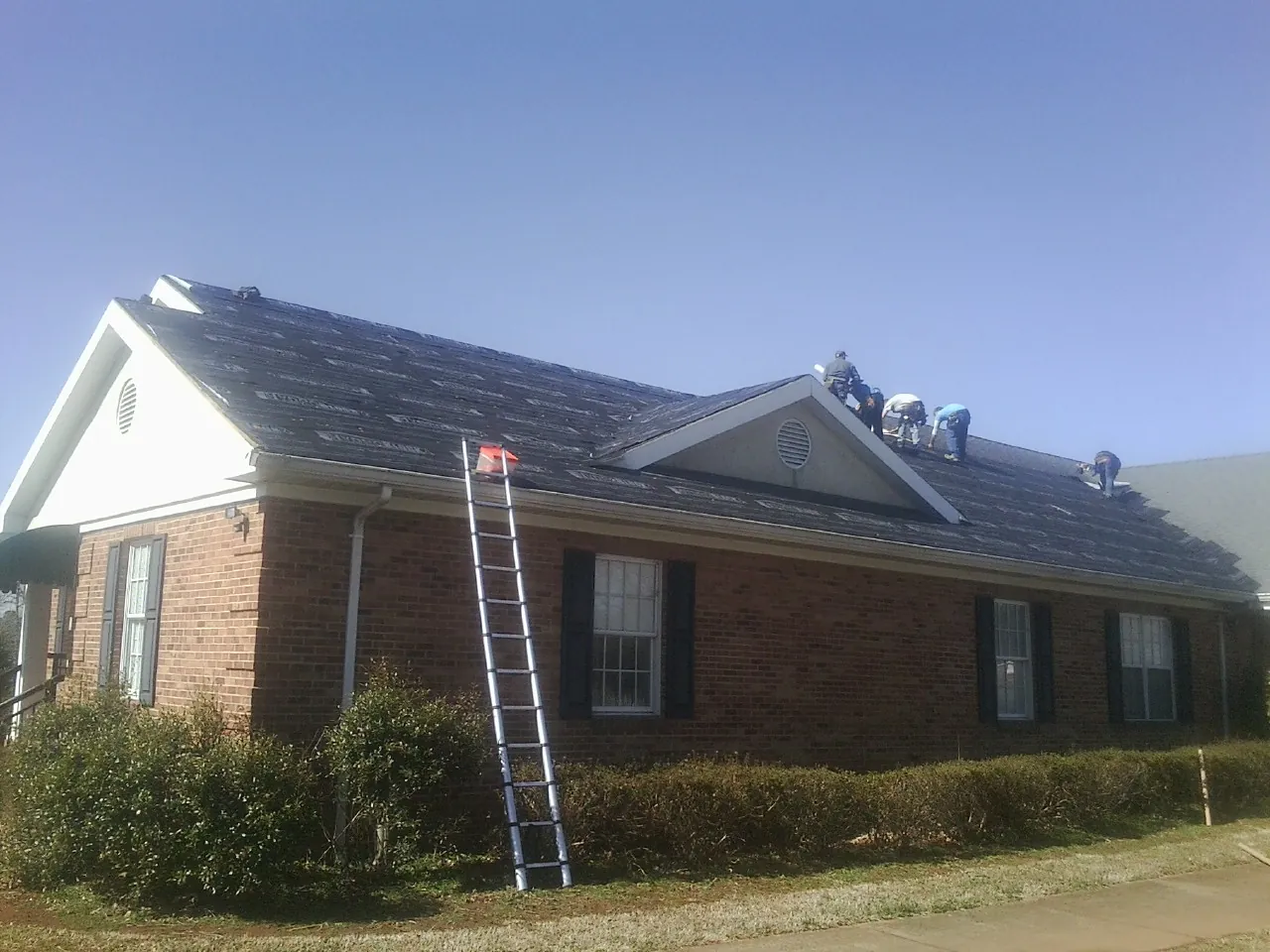 Crew tearing shingles off a brick ranch roof with a ladder set — Emergency Roof Repair work by our crew in Fort George G Meade
