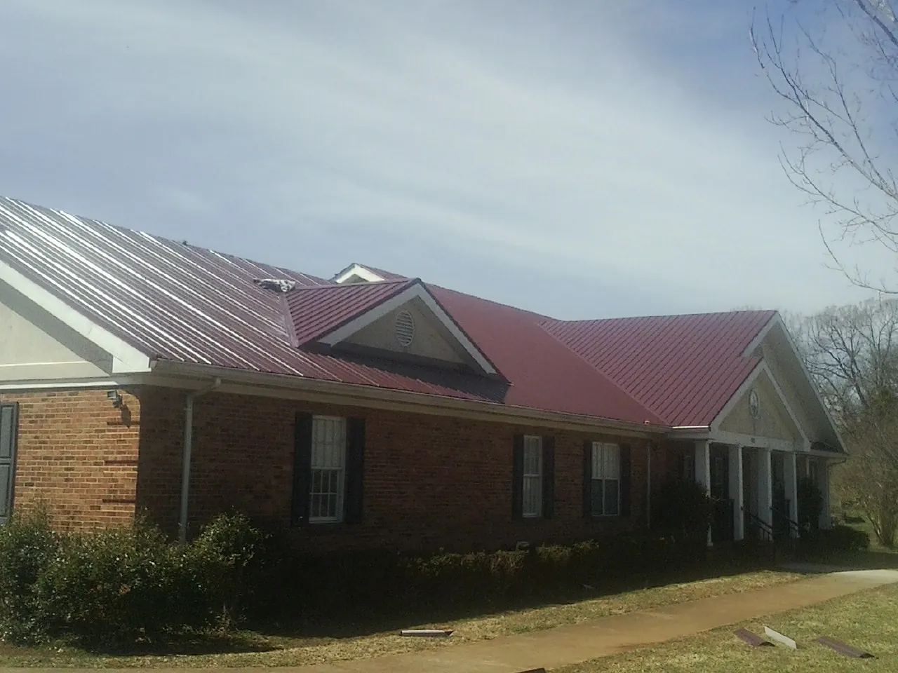 Red metal roof with gabled entries on a long brick building, from a Hail Damage Roof Repair job in Fort George G Meade