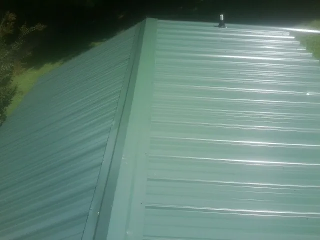 New green metal panels meeting at the ridge of a roof — Flat Roof Repair work by our crew in Fort George G Meade