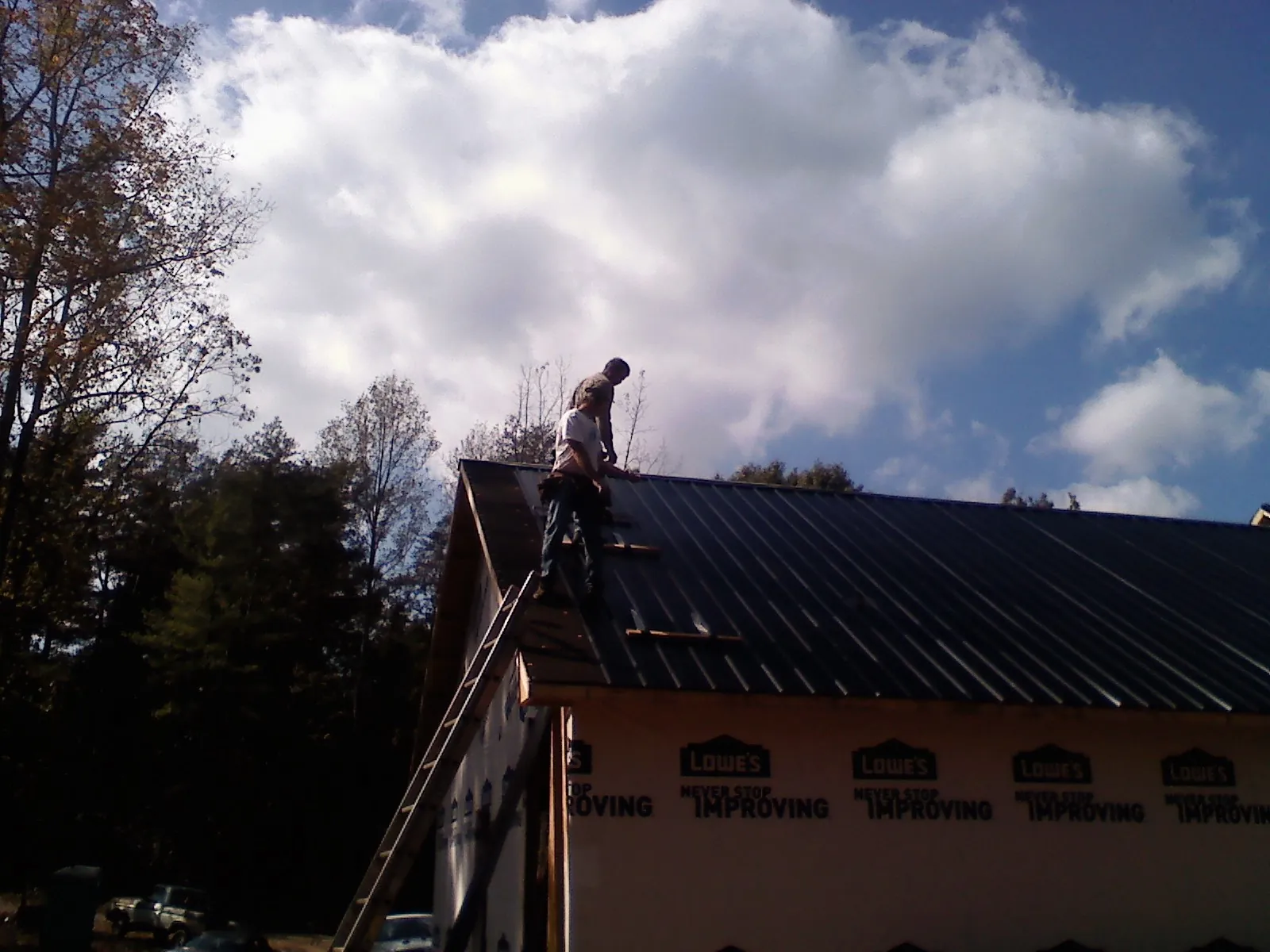 Roofer fastening dark metal panels high against a cloudy sky, from a Roof Inspection job in Fort George G Meade