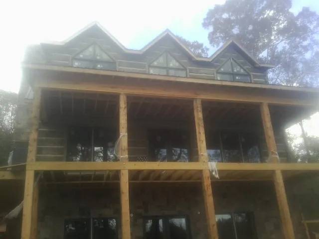 Dormers and porch framing on a large log home under construction — Roof Coating work by our crew in Fort George G Meade