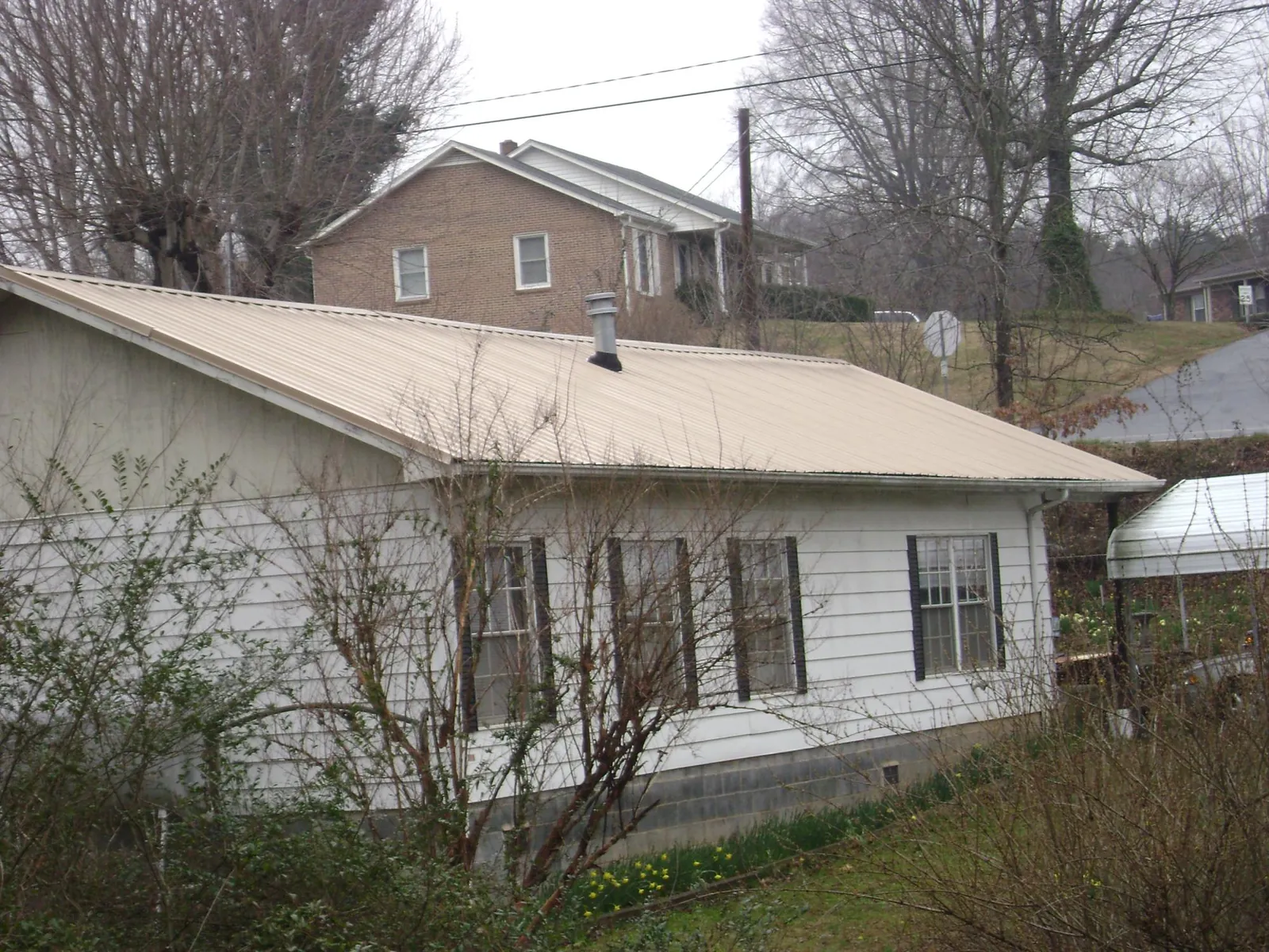 Tan metal roof on a white sided house set into a hillside — Commercial Roofing by Roofing Brothers in Fort George G Meade